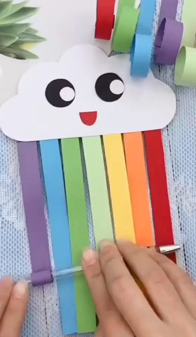 Le nuage arc-en-ciel avec son visage collé, dont on enroule les bandes de couleur autour d'un crayon pour les faire boucler